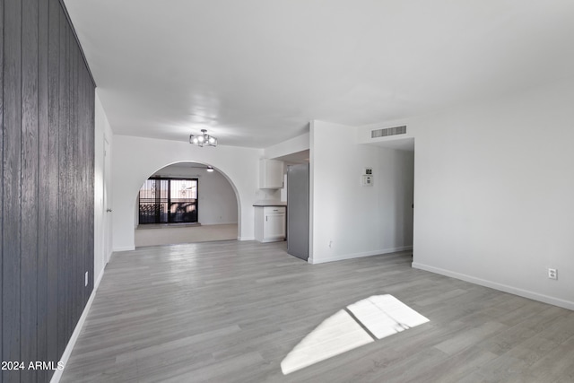 unfurnished living room with a chandelier, wood walls, and light hardwood / wood-style flooring