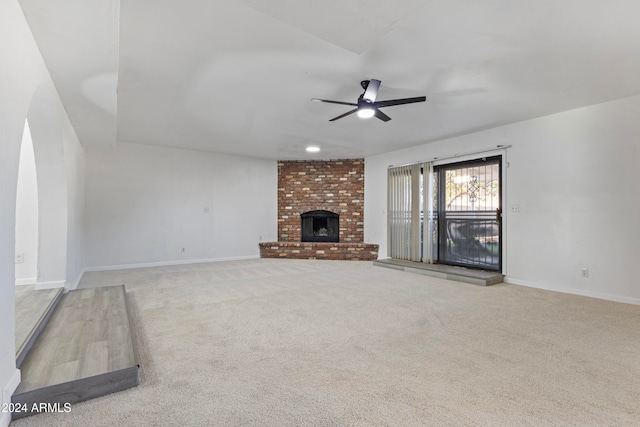 unfurnished living room with ceiling fan, light colored carpet, and a brick fireplace