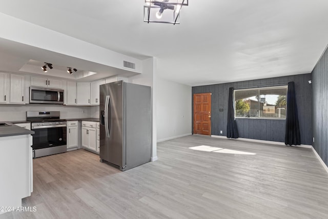 kitchen featuring appliances with stainless steel finishes, light hardwood / wood-style flooring, white cabinetry, and wood walls