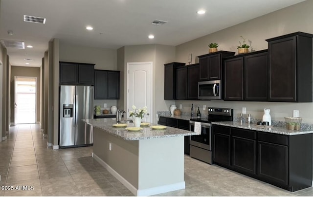 1255 N Arizona Ave Unit 1235, Chandler, AZ 85225 - kitchen featuring appliances with stainless steel finishes, light stone counters, a kitchen island with sink, dark cabinetry, and light tile patterned floors