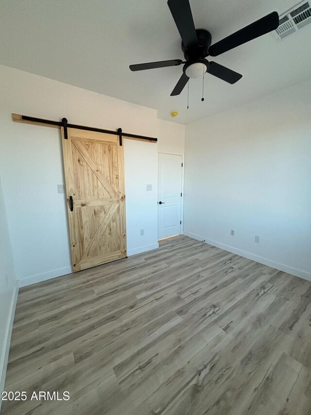 3627 W Palmaire Ave, Phoenix, AZ 85051 - unfurnished bedroom featuring wood finished floors, baseboards, a barn door, and a ceiling fan