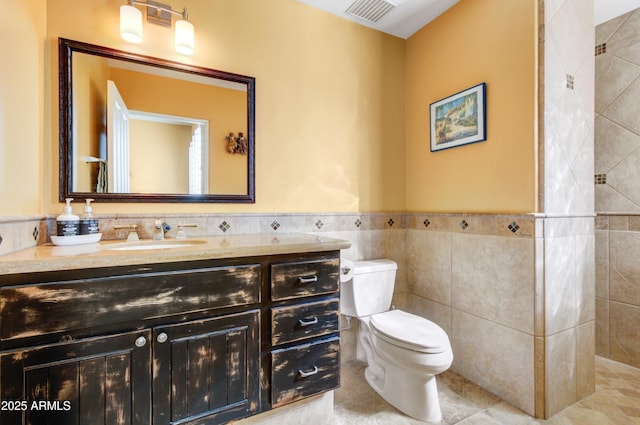 bathroom featuring visible vents, toilet, a wainscoted wall, vanity, and tile walls