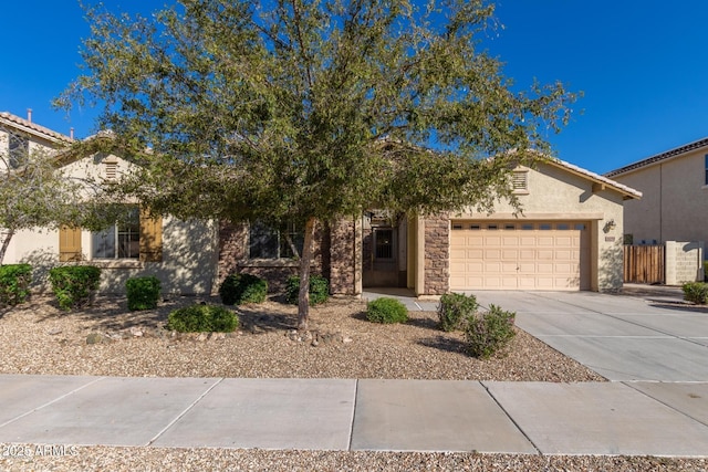 16758 W Apache St, Goodyear, AZ 85338 - view of property hidden behind natural elements featuring concrete driveway, a garage, stucco siding, and stone siding