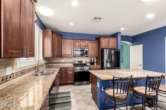 81 E Rock Wren Dr, San Tan Valley, AZ 85143 - kitchen with appliances with stainless steel finishes, a sink, light stone counters, decorative backsplash, and a breakfast bar area