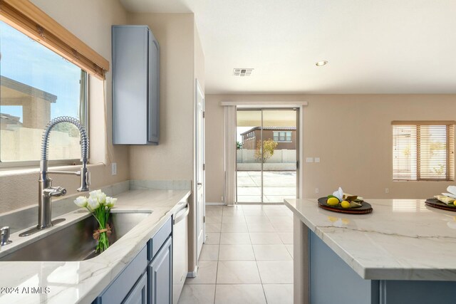 kitchen with light tile patterned floors, light stone counters, plenty of natural light, and sink