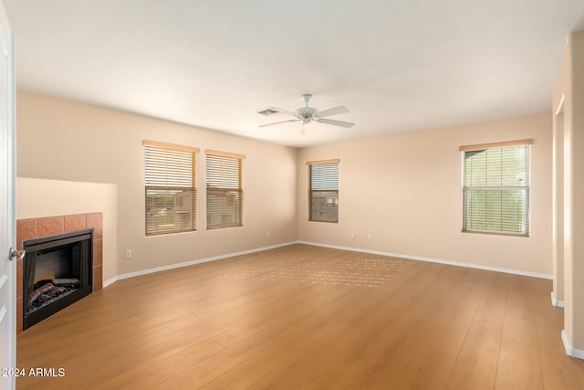 unfurnished living room featuring a tiled fireplace, ceiling fan, and light hardwood / wood-style floors