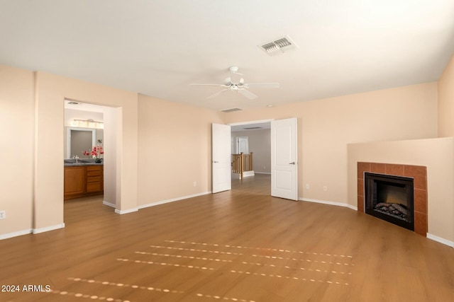 unfurnished living room featuring wood-type flooring, ceiling fan, and a tiled fireplace