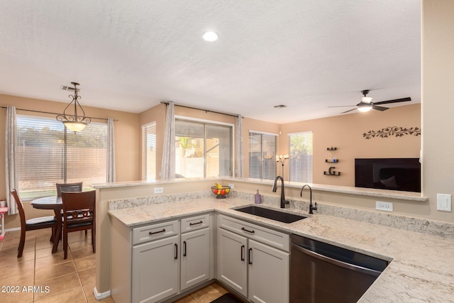 kitchen with light stone countertops, sink, stainless steel dishwasher, and decorative light fixtures