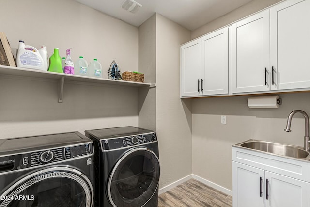 laundry area featuring light hardwood / wood-style floors, sink, washing machine and dryer, and cabinets