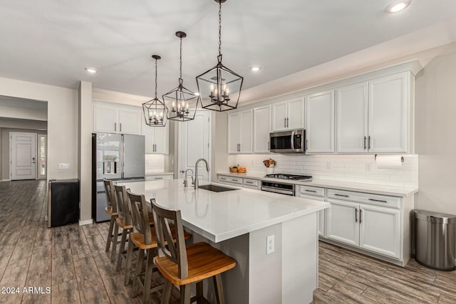 kitchen with white cabinetry, sink, hanging light fixtures, stainless steel appliances, and a center island with sink