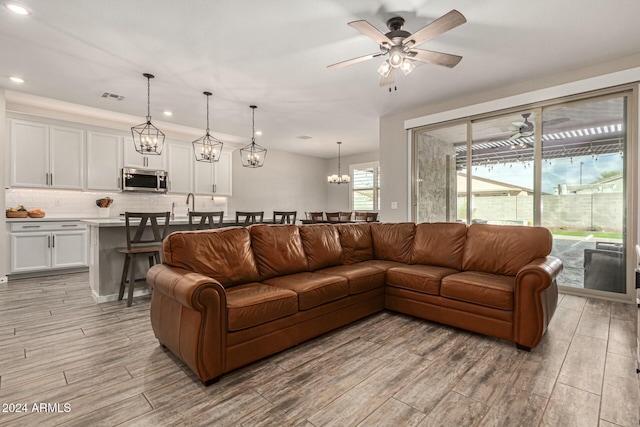 living room featuring ceiling fan with notable chandelier and light hardwood / wood-style flooring