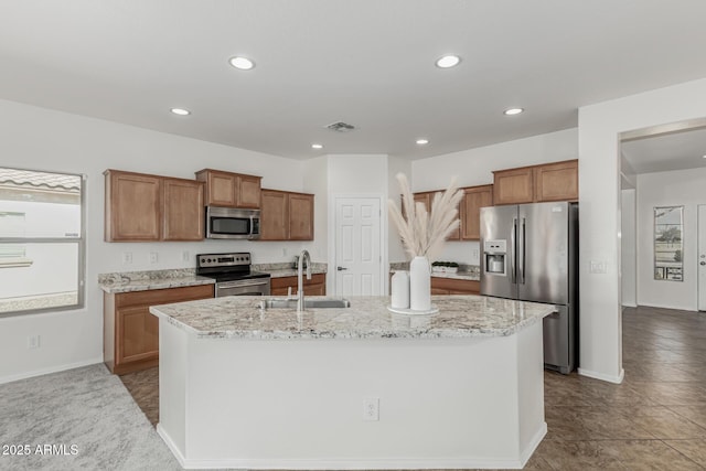 kitchen featuring sink, appliances with stainless steel finishes, an island with sink, and light stone counters