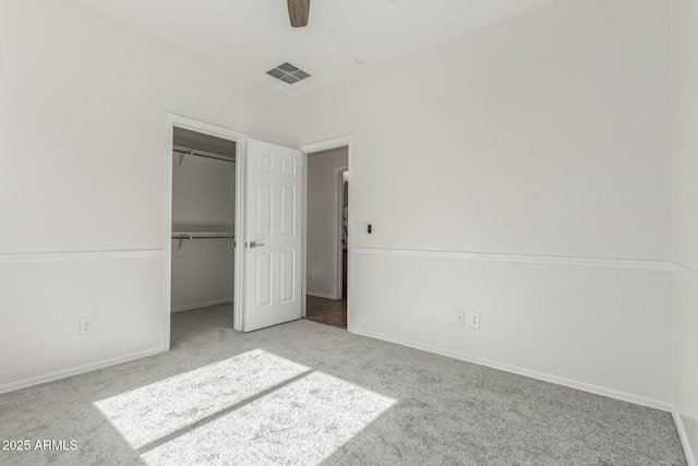 unfurnished bedroom with light carpet, a spacious closet, ceiling fan, and a closet