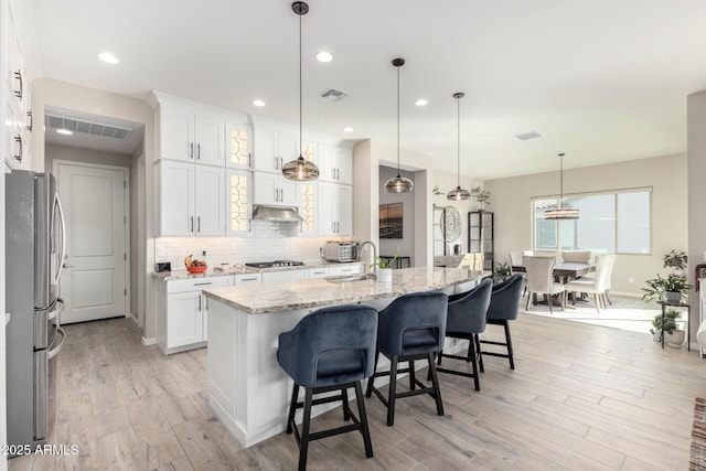 kitchen with a center island with sink, a kitchen breakfast bar, white cabinets, light stone countertops, and stainless steel appliances