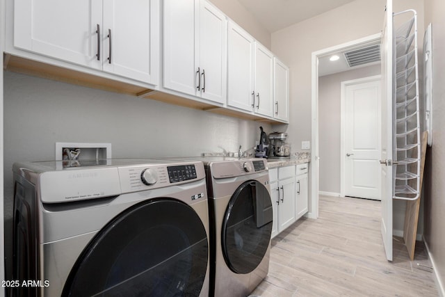 laundry room with washing machine and dryer, light hardwood / wood-style flooring, and cabinets