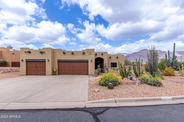pueblo revival-style home with concrete driveway, a garage, stucco siding, and a mountain view