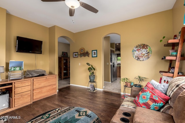 living area with ceiling fan, dark wood-style flooring, arched walkways, and baseboards