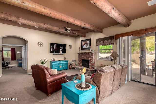 carpeted living area with beamed ceiling, arched walkways, and a wealth of natural light