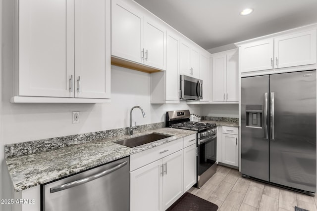 kitchen with white cabinets, appliances with stainless steel finishes, light stone counters, and sink