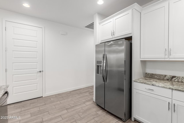 kitchen with stainless steel refrigerator with ice dispenser, white cabinetry, and light stone counters