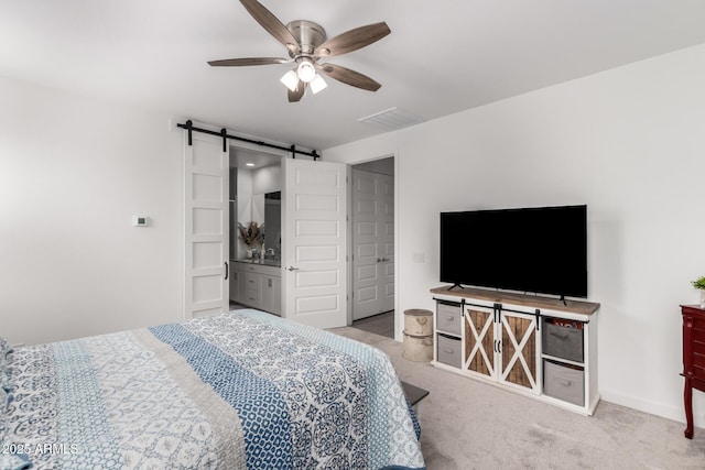 bedroom with connected bathroom, a barn door, ceiling fan, and light carpet