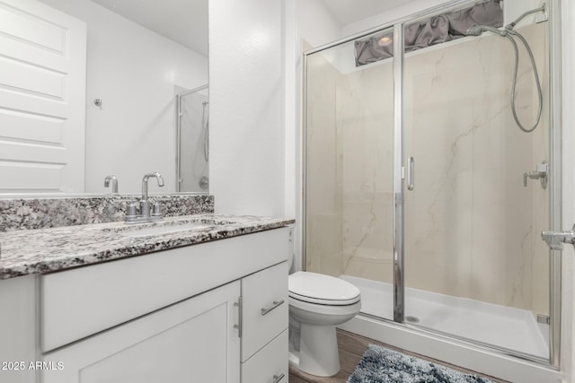 bathroom with hardwood / wood-style floors, vanity, toilet, and a shower with shower door