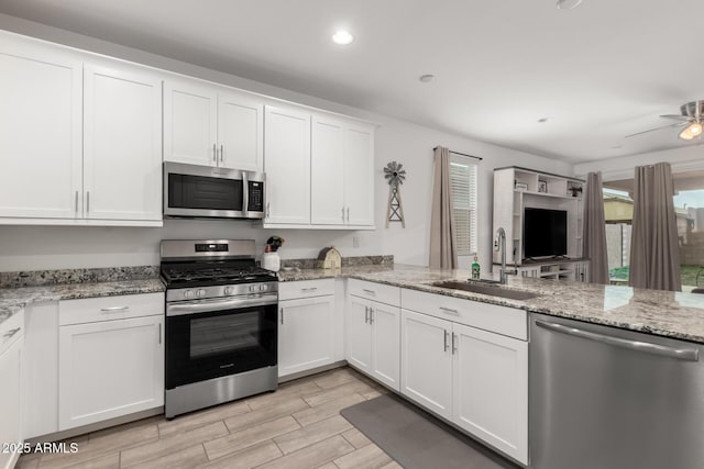 kitchen with sink, light stone counters, kitchen peninsula, white cabinets, and appliances with stainless steel finishes