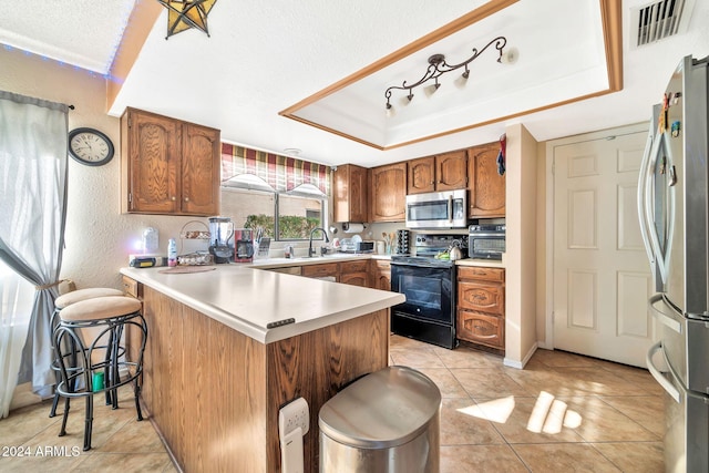 kitchen featuring a raised ceiling, kitchen peninsula, a breakfast bar, and stainless steel appliances