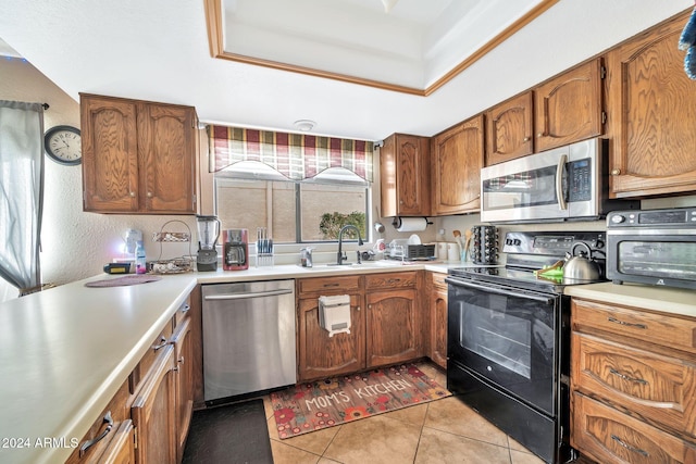 kitchen featuring light tile patterned flooring, appliances with stainless steel finishes, a tray ceiling, and sink