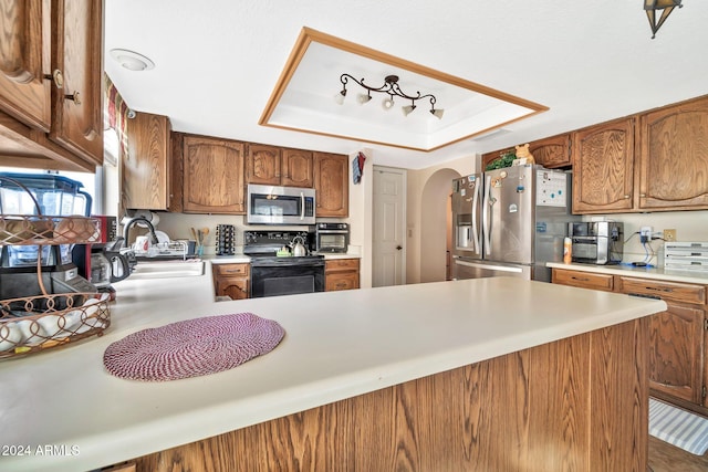 kitchen with a tray ceiling, kitchen peninsula, sink, and appliances with stainless steel finishes