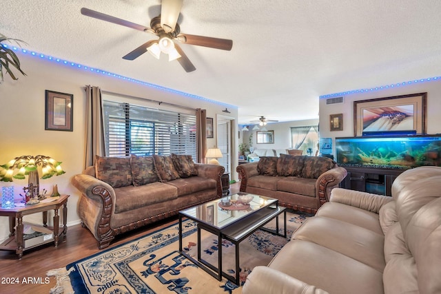 living room with a textured ceiling, ceiling fan, and dark wood-type flooring