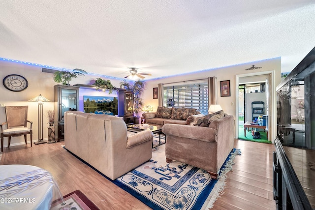 living room with ceiling fan, light wood-type flooring, and a textured ceiling