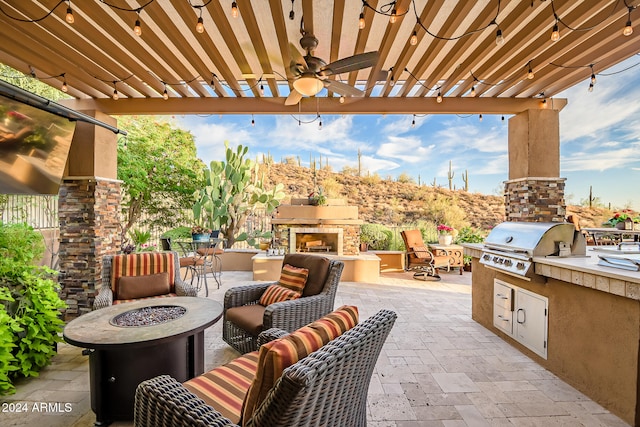 view of patio / terrace featuring area for grilling, ceiling fan, an outdoor stone fireplace, and exterior kitchen