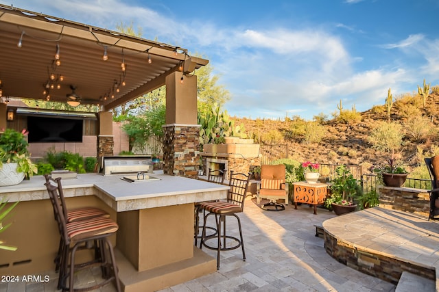 view of patio / terrace featuring ceiling fan, exterior kitchen, an outdoor bar, and an outdoor stone fireplace