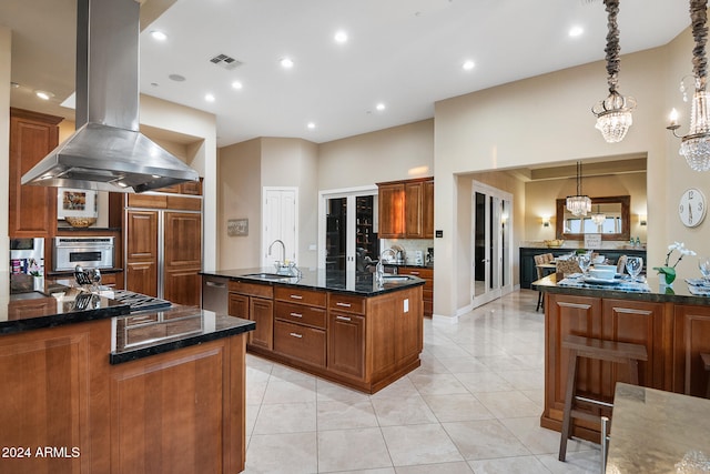 kitchen with sink, island range hood, stainless steel appliances, decorative light fixtures, and a center island with sink