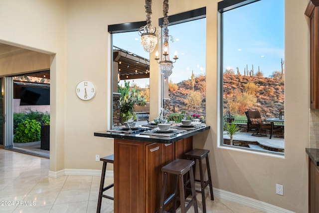 kitchen featuring kitchen peninsula, light tile patterned floors, a breakfast bar area, a chandelier, and pendant lighting