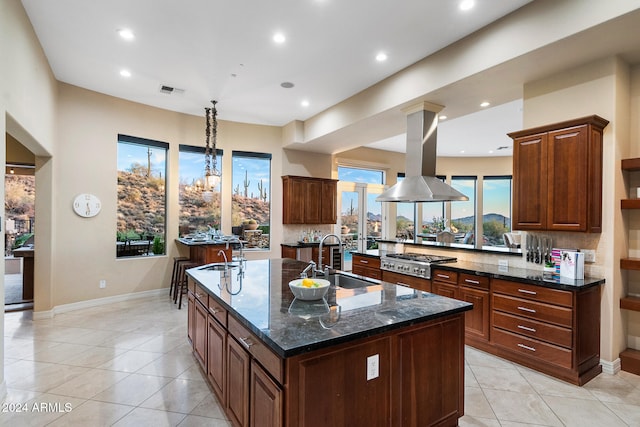 kitchen featuring stainless steel gas cooktop, backsplash, island exhaust hood, light tile patterned floors, and a kitchen island with sink