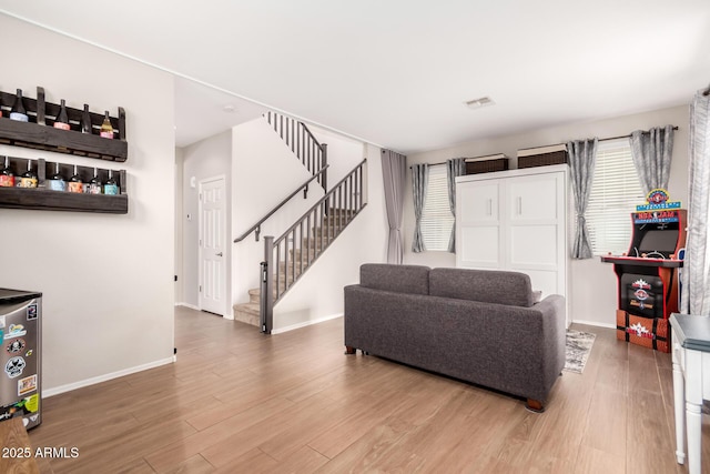 living room featuring baseboards, visible vents, stairway, and wood finished floors