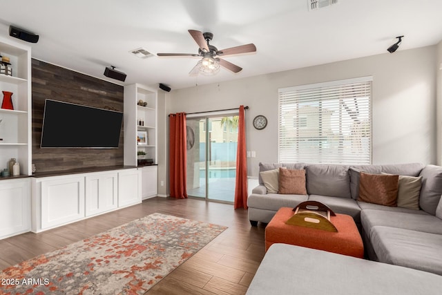 living room featuring a ceiling fan, visible vents, built in shelves, and wood finished floors