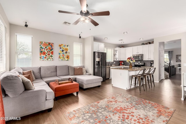 living area featuring a ceiling fan, a healthy amount of sunlight, visible vents, and wood finished floors