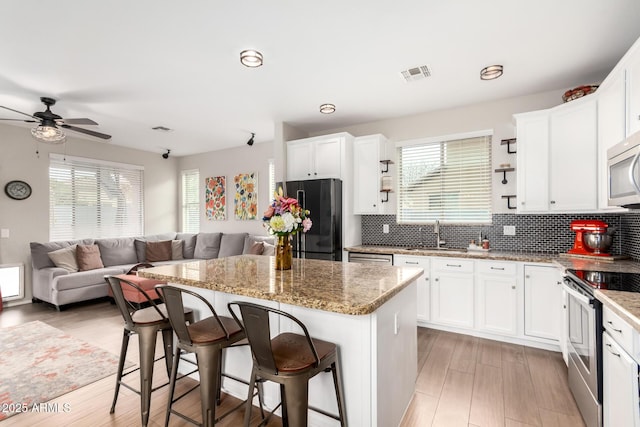 kitchen with stainless steel appliances, a kitchen island, visible vents, open floor plan, and backsplash