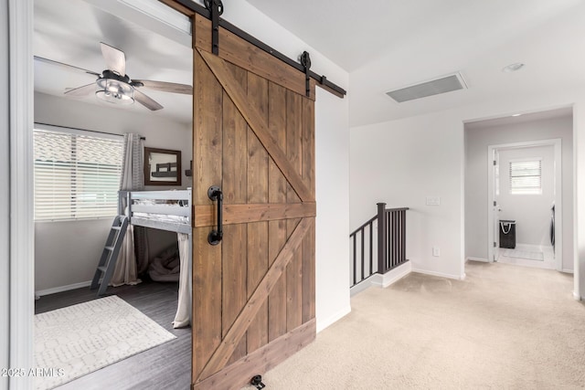 corridor featuring an upstairs landing, a barn door, baseboards, and light colored carpet