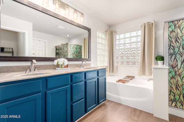 full bath featuring a garden tub, double vanity, wood finished floors, and a sink