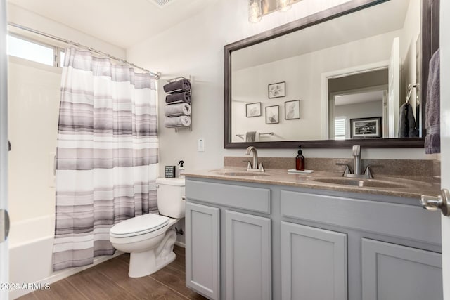 bathroom featuring toilet, double vanity, a sink, and wood finished floors