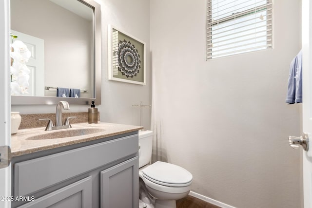 half bath with toilet, baseboards, and vanity