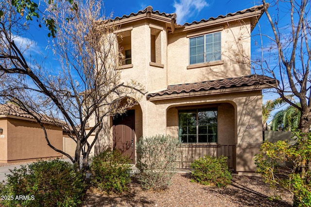 mediterranean / spanish home with fence, a tiled roof, and stucco siding