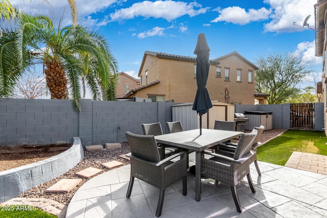 view of patio with outdoor dining space, a gate, a shed, a fenced backyard, and an outdoor structure