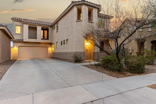 mediterranean / spanish-style house featuring concrete driveway, a balcony, a tiled roof, an attached garage, and stucco siding