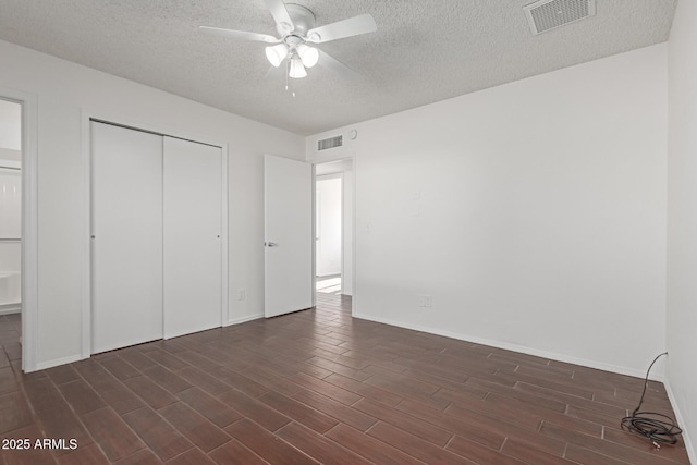 unfurnished bedroom featuring a textured ceiling, dark wood-style flooring, visible vents, baseboards, and a closet