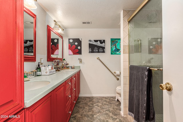 bathroom featuring a textured ceiling, vanity, toilet, and a shower with shower door